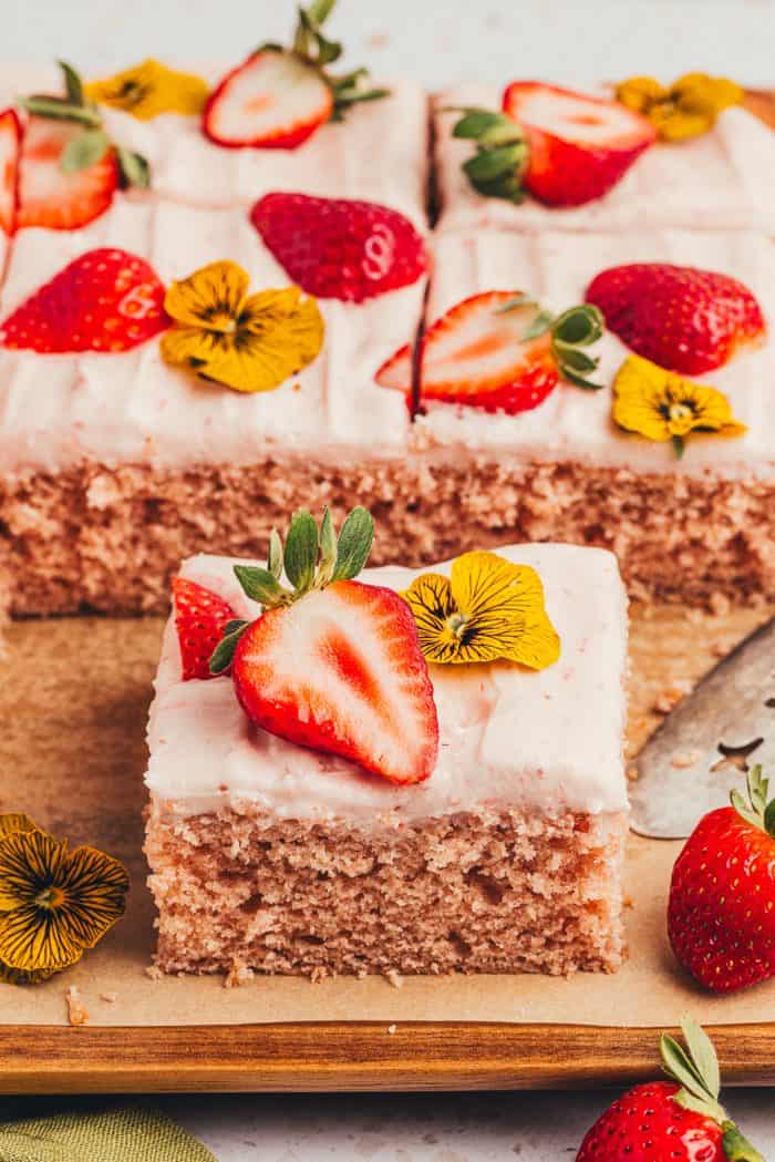 Slices of strawberry sheet cake on a wooden board.