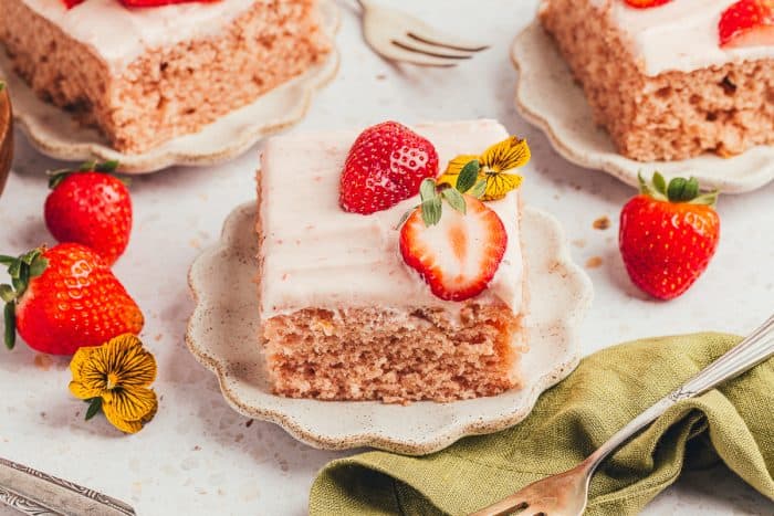 Three slices of strawberry sheet cake on plates with strawberries around them.
