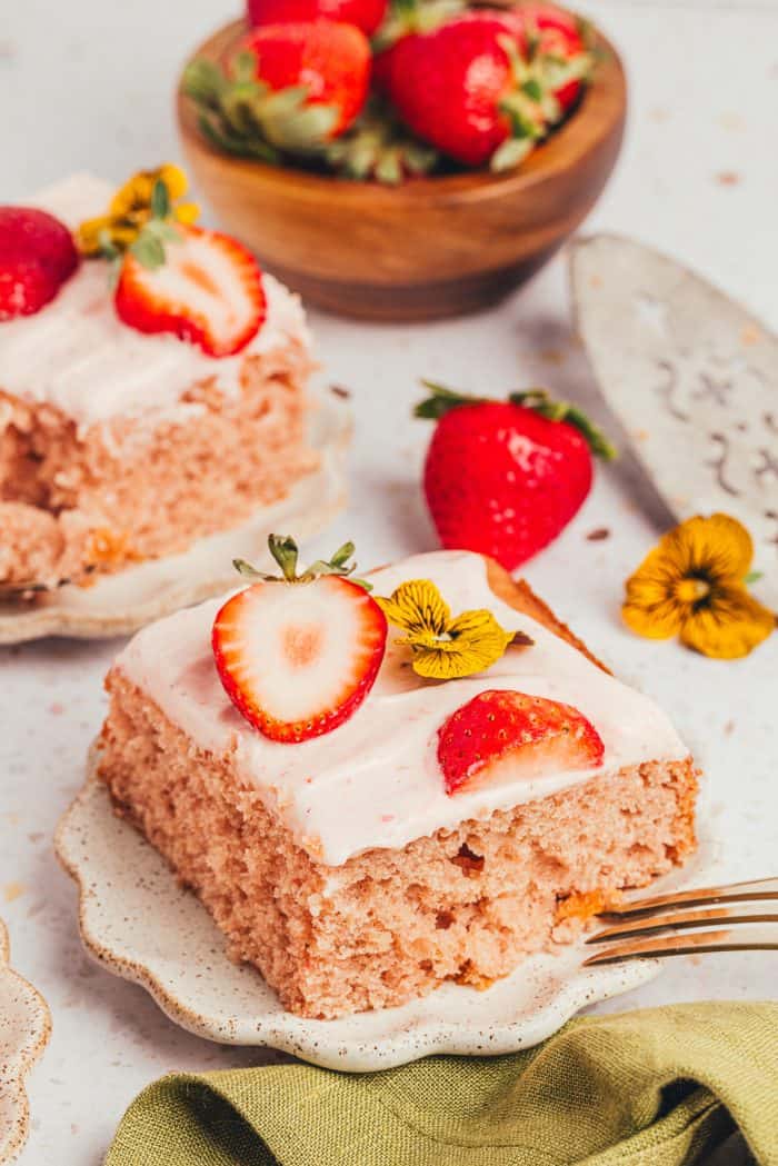 Three slices of strawberry sheet cake on plates with strawberries around them.