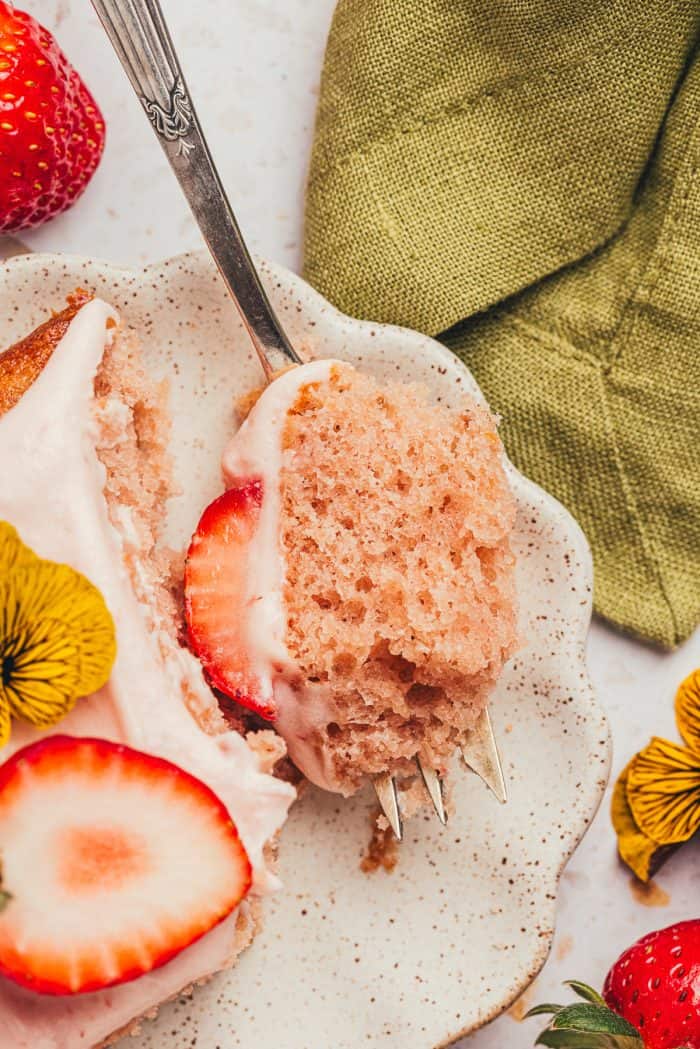 A slice of strawberry sheet cake on a plate with a fork piercing it.